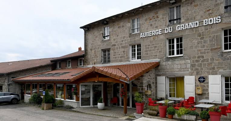 Façade en pierre de l’Auberge du Grand Bois à La Versanne, avec son enseigne et son entrée sous un auvent.