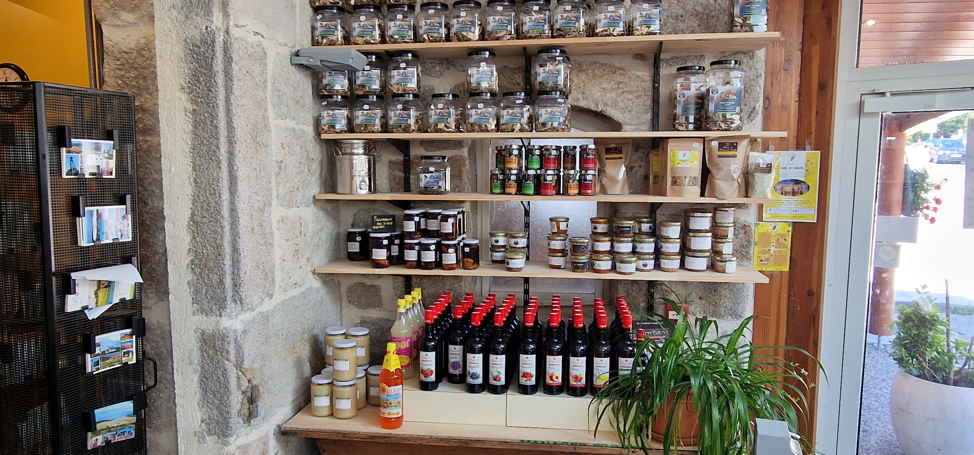 Étagères de produits régionaux dans la boutique de l’Auberge du Grand Bois, devant un mur en pierre. Photo du site officiel du prestataire.